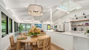 A spacious kitchen with a central island, white cabinetry, and a large window overlooking a garden.