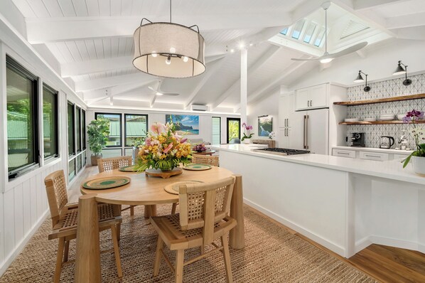 A spacious kitchen with a central island, white cabinetry, and a large window overlooking a garden.