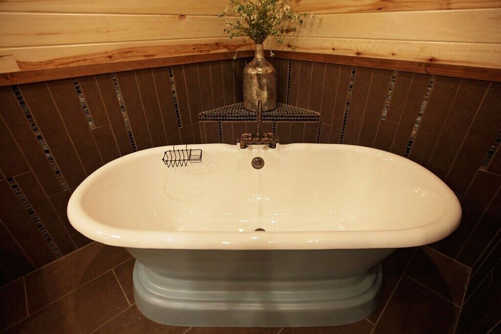 Eine weiße, freistehende Badewanne in einem Badezimmer mit Holzwand und dekorativer Vase.