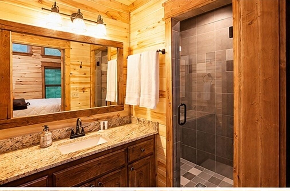 A wooden cabin-style bathroom with a large mirror, a sink, and a shower.