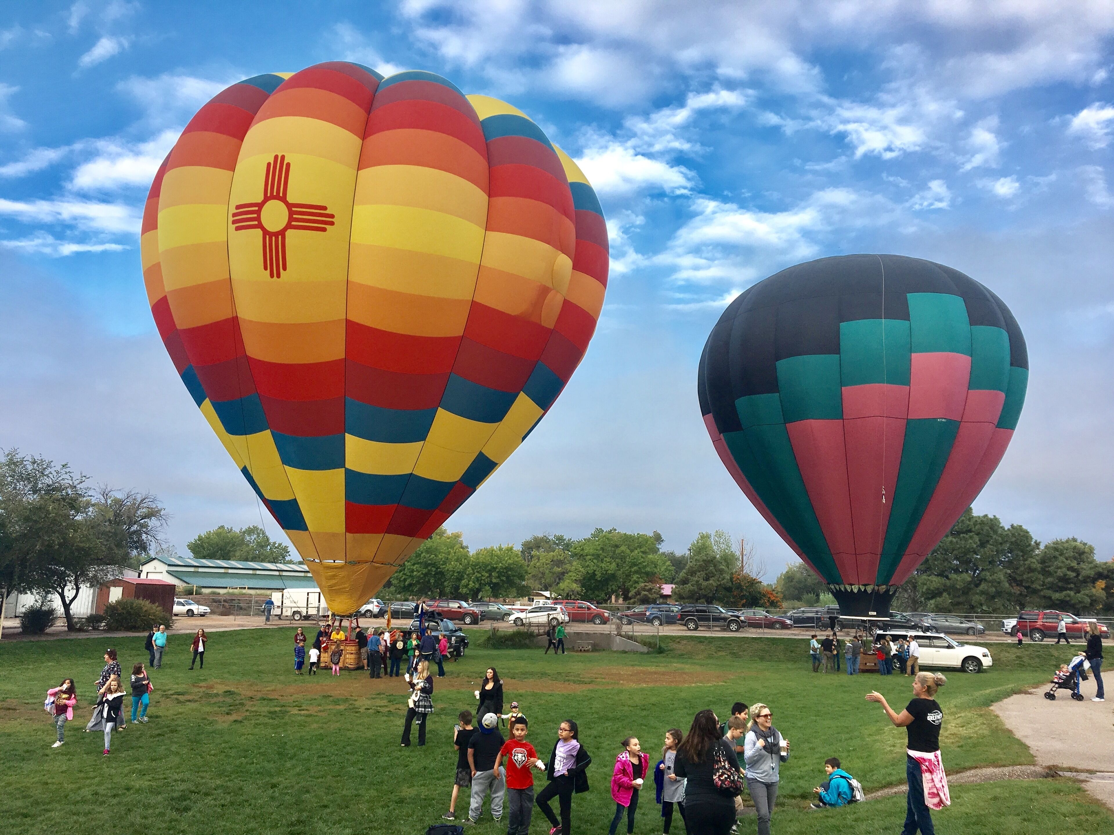 Zwei große Heißluftballons in einem grünen Feld, umgeben von Menschen.