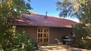 Un edificio con techo de metal rojo, una puerta de madera y una parrilla de barbacoa en el exterior.