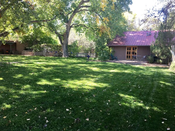 A grassy yard with a building that has a red roof and a wooden door. - Oasis in the City.  1 BD,  1 BA.  ABQ, NM (Albuquerque)