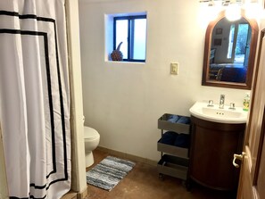 A bathroom with a toilet, a small window, a sink with a mirror, and a storage cart. - Oasis in the City.  1 BD,  1 BA.  ABQ, NM (Albuquerque)