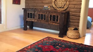 Una habitación con un banco de madera apoyado en una pared de ladrillo, un tapiz tejido y una alfombra estampada sobre un suelo de madera.