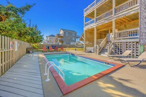 A swimming pool with a wooden deck, lounge chairs, and a wooden fence.