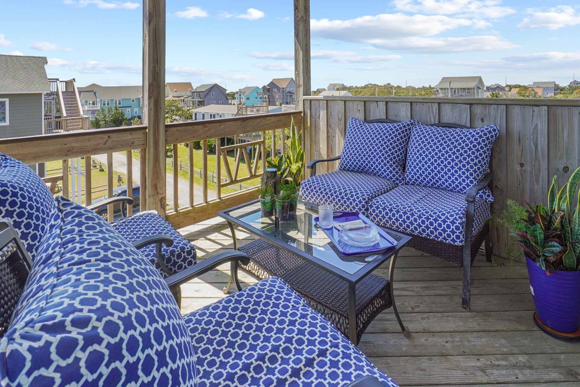 A covered outdoor seating area with a wooden deck, a glass table, and patterned cushions.
