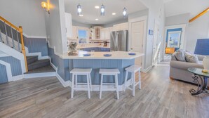 A modern kitchen with a central island, white bar stools, and pendant lighting. - Semi-Oceanfront Dog Friendly Home w/ Pool, Hot Tub, Game Room, Fenced Yard (Salvo)