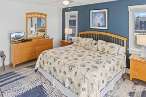 A bedroom with a large bed, wooden headboard, a dresser, a mirror, and a window with a view.