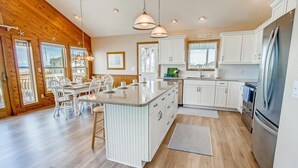 A modern kitchen with white cabinetry, a central island, and a large refrigerator. - Semi-Oceanfront Home w/ Private Pool, Hot Tub, Basketball. Watch the Waves Crest (Waves)