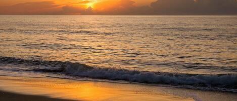 A beach at sunset with waves approaching the shore.