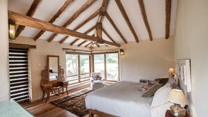 Ein Schlafzimmer mit einem großen Bett, Holzbalken, einem Fenster, einem Sessel und einem Spiegel.