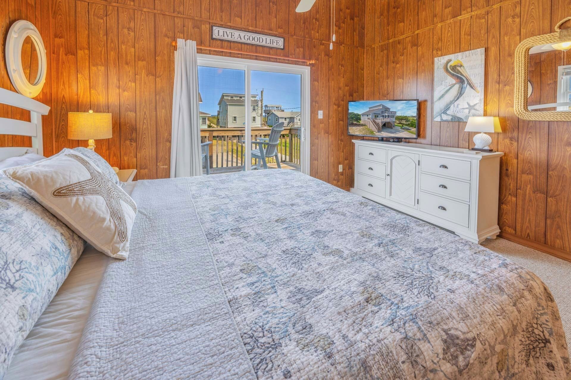 Ein Schlafzimmer mit einem großen Bett, einem Fernseher, einer Holzwand und einem Balkon mit Blick auf Häuser.