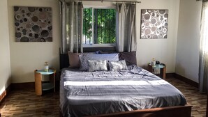 Un dormitorio con una cama, dos mesitas de noche, una ventana con cortinas y obras de arte en las paredes.
