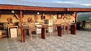 Un espacio de cocina al aire libre con una barra larga, taburetes y vistas al paisaje circundante.