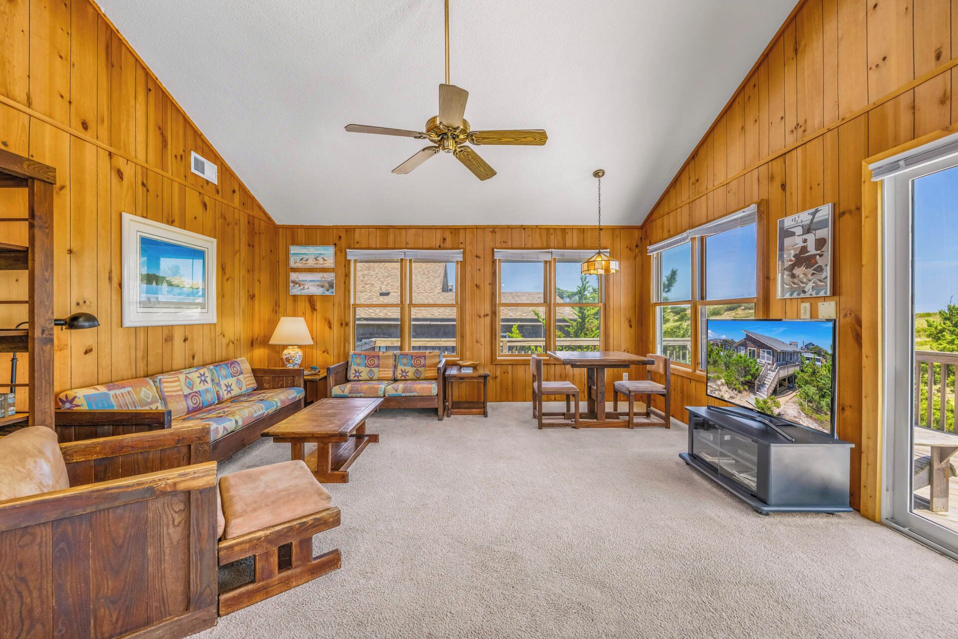 A room with wooden paneling, a ceiling fan, a sofa set, a dining table with chairs, and a television.