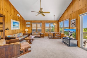 A room with wooden paneling, a ceiling fan, a sofa set, a dining table with chairs, and a television. - Oceanfront Home with Direct Beach Access, Community Pool and Tennis/Pickleball (Avon)
