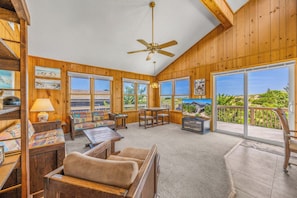 A spacious room with a ceiling fan, large windows, a TV, and a view of the outdoors. - Oceanfront Home with Direct Beach Access, Community Pool and Tennis/Pickleball (Avon)