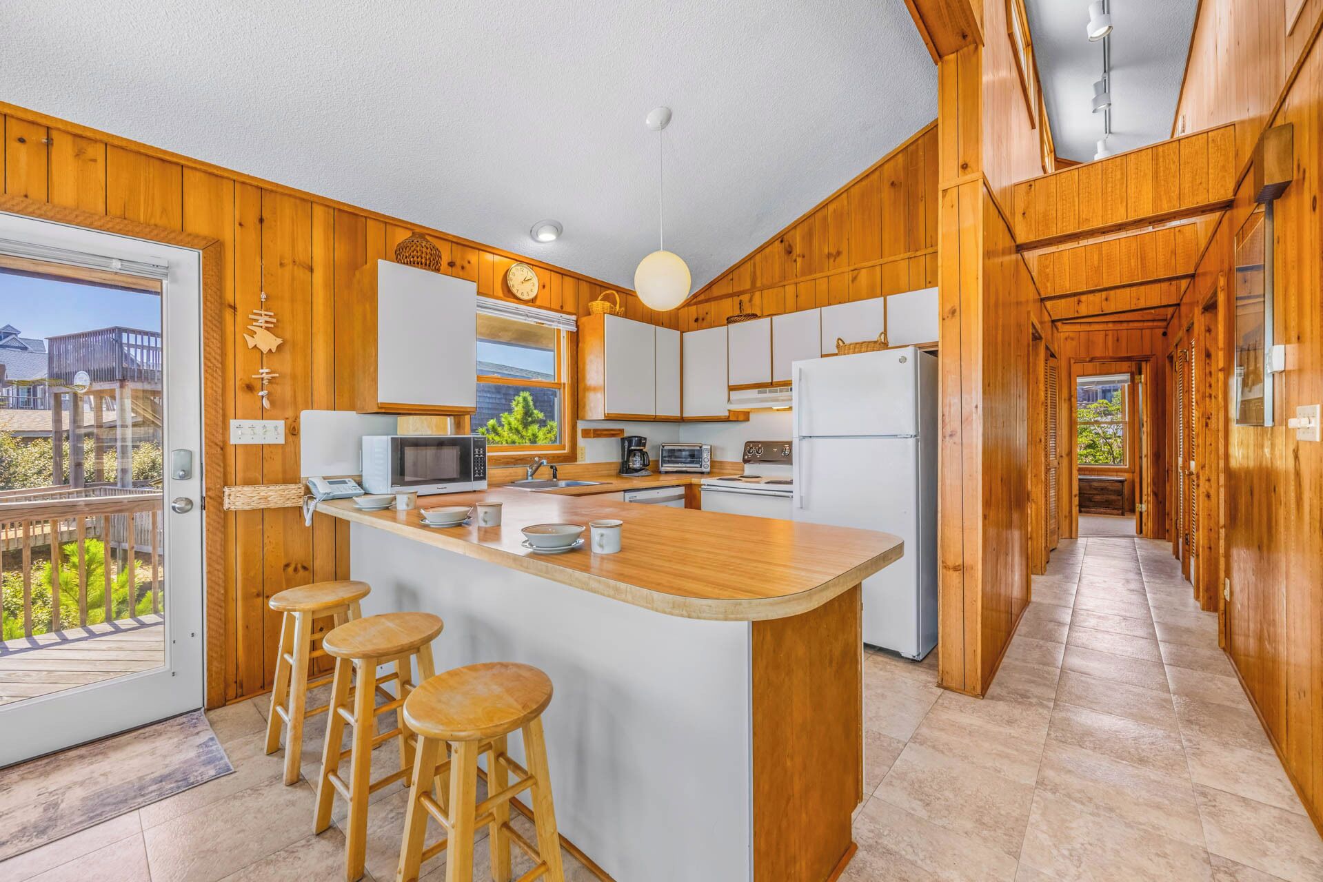 A kitchen with wooden paneling, a central island with stools, and a view through the door.