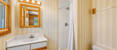 A bathroom with a vanity, mirror, shower, and toilet.