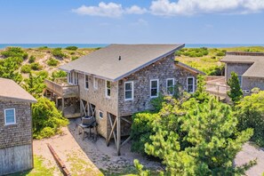 A wooden house with a balcony, surrounded by greenery and a view of the ocean. - Oceanfront Home with Direct Beach Access, Community Pool and Tennis/Pickleball (Avon)