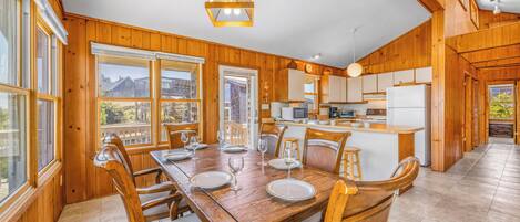 A wooden interior with a dining table set for four, kitchen area with appliances, and large windows.