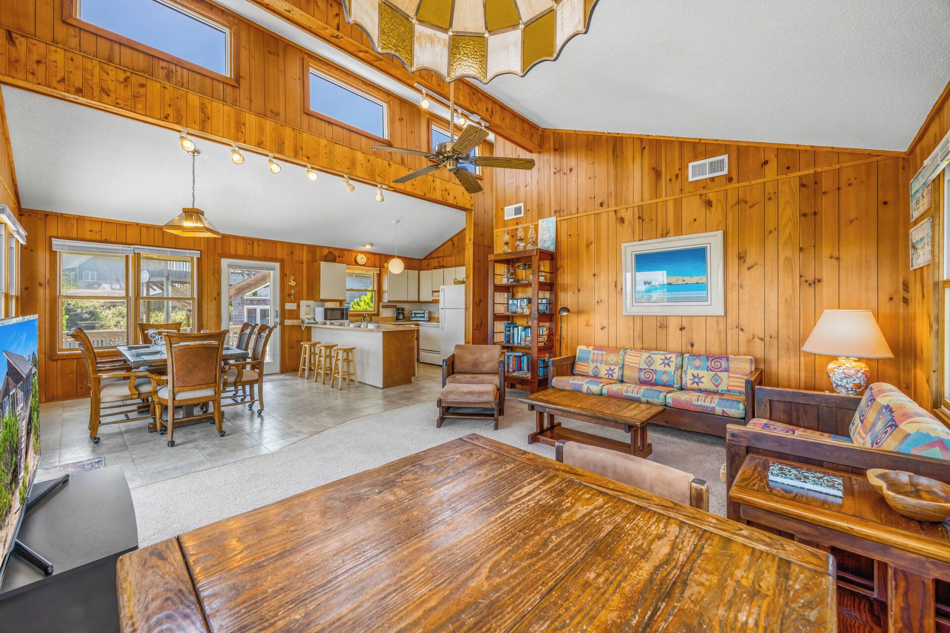 A spacious living area with a wooden interior, a dining table, a sofa, and a kitchen in the background.
