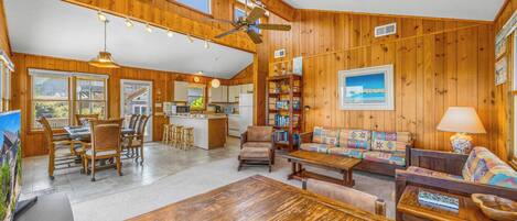 A spacious living area with a wooden interior, a dining table, a sofa, and a kitchen in the background.