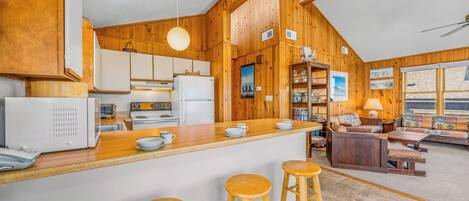 A kitchen with wooden cabinets, a white refrigerator, a stove, and a bar area with stools.