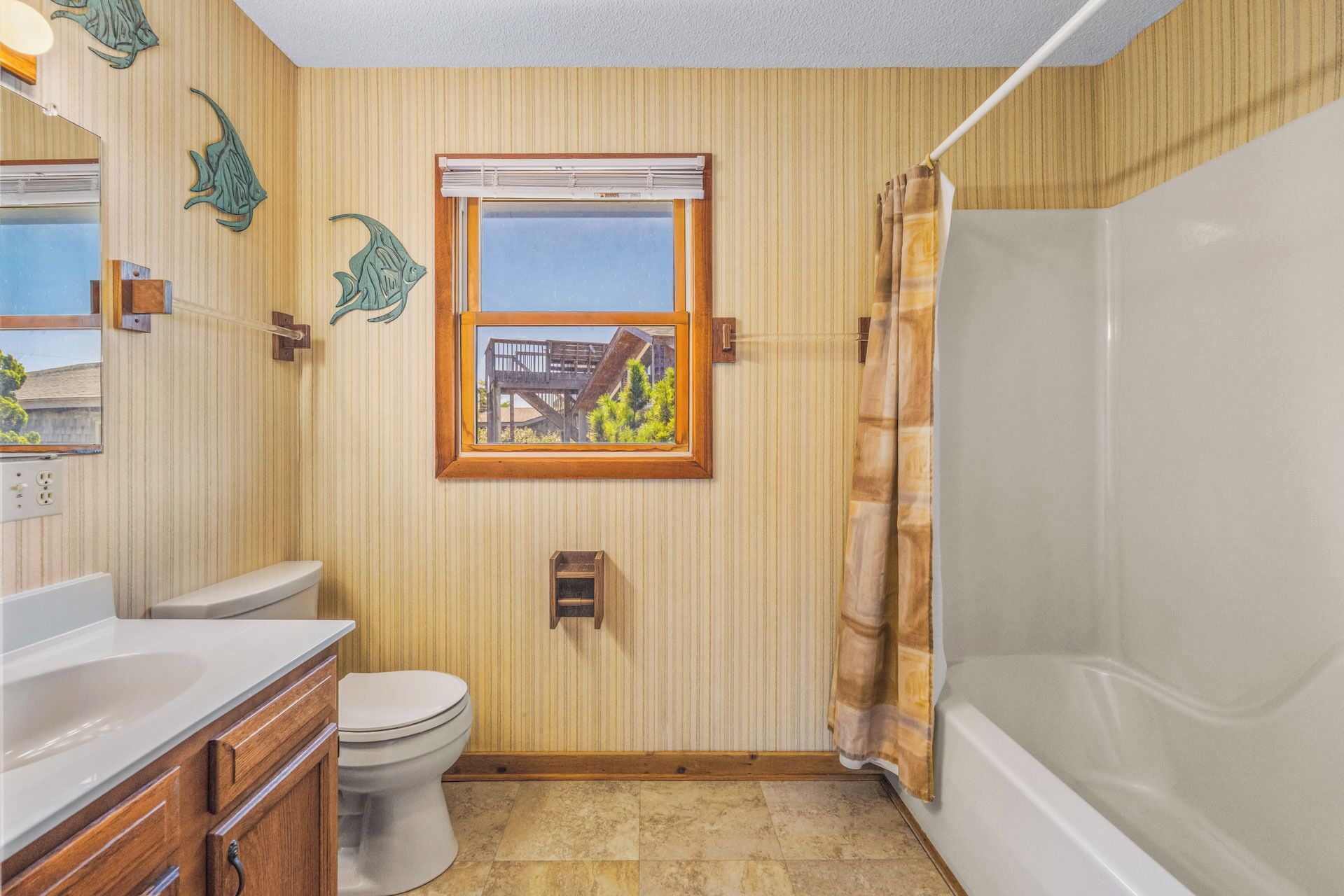 A bathroom with a toilet, vanity, bathtub, and a window with a view of buildings.