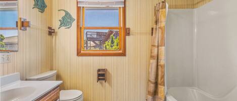 A bathroom with a toilet, vanity, bathtub, and a window with a view of buildings.