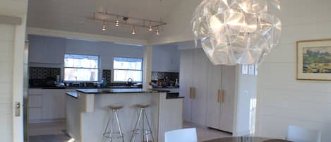 A modern kitchen with a central island, bar stools, and a dining area with a glass table and chairs.