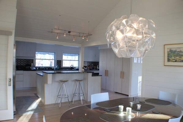 A modern kitchen with a central island, bar stools, and a dining area with a glass table and chairs.