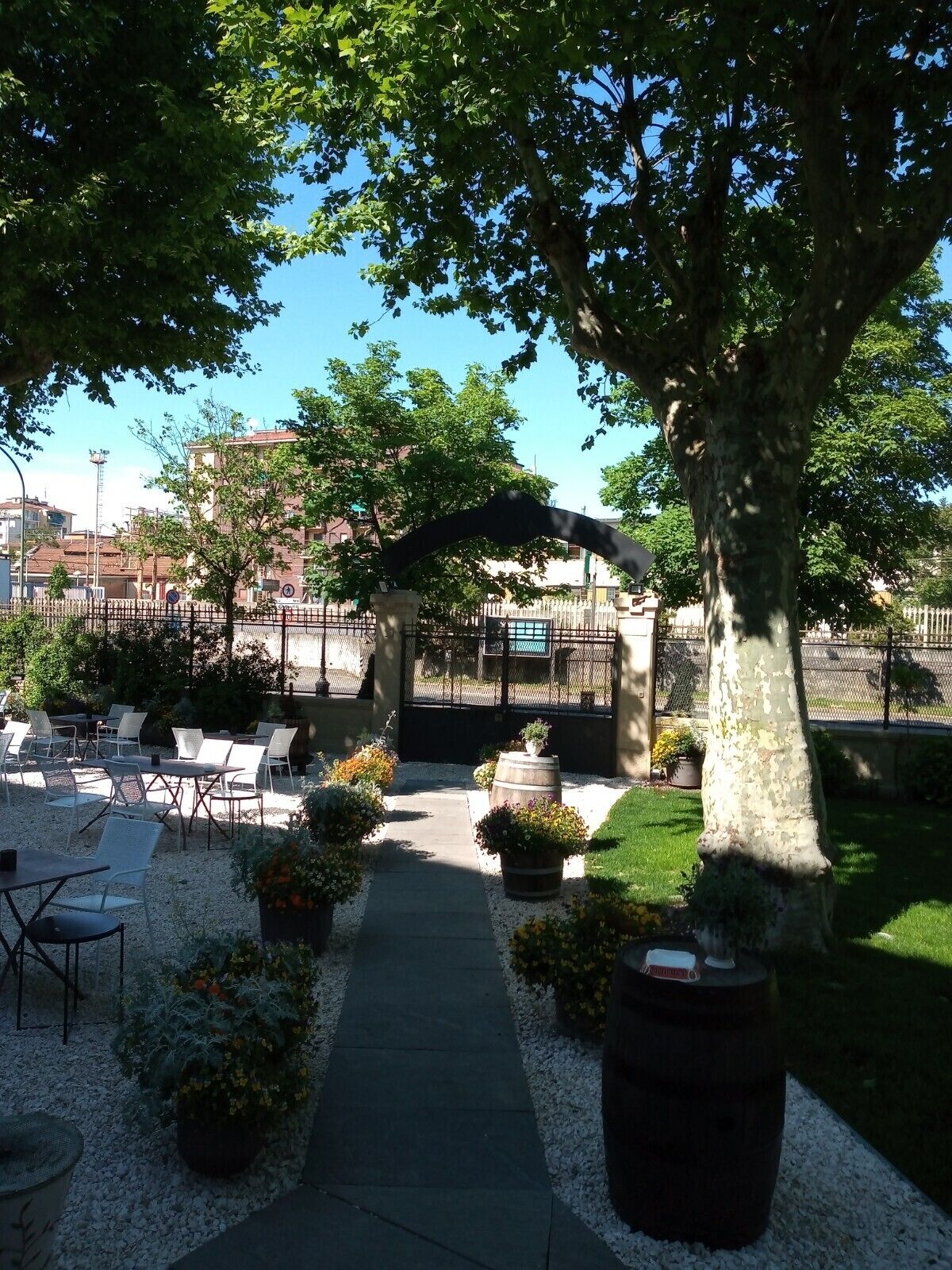 An outdoor seating area with tables and chairs, surrounded by trees and a pathway.