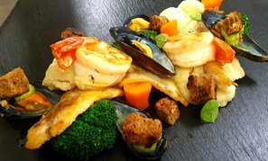 A seafood dish with mussels, shrimp, and vegetables on a slate plate.