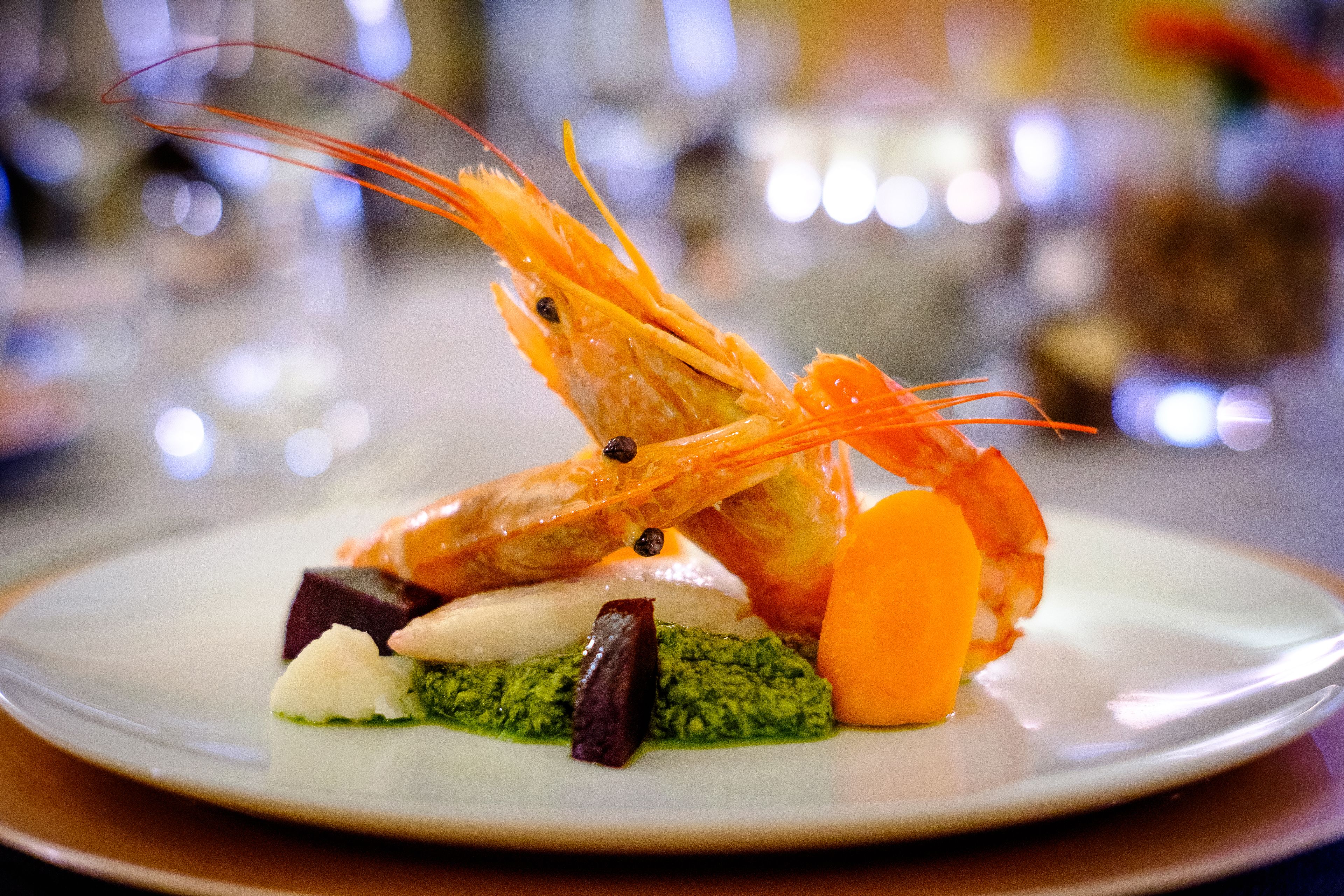 A plate with a shrimp, a carrot, and some greens.