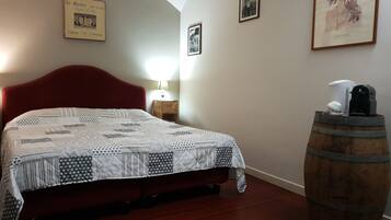 A bedroom with a red headboard, a quilted bedspread, a wooden barrel, and framed pictures on the wall.