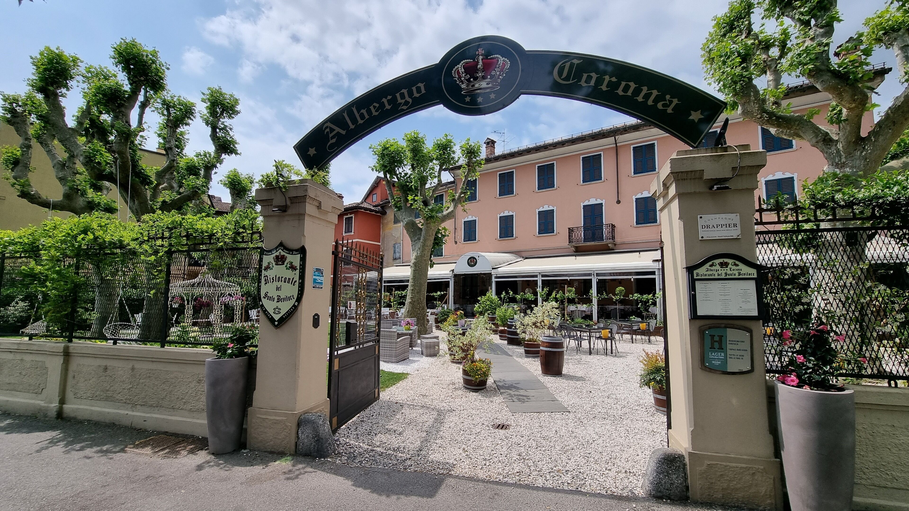 A hotel entrance with a sign reading "Albergo Corona" and a traditional building in the background.