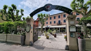 A hotel entrance with a sign reading "Albergo Corona" and a traditional building in the background.