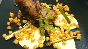 Een gebraden lamsbout met geroosterde aardappelen en asperges, gepresenteerd op een zwarte leisteenplaat.