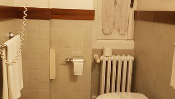 Un baño con dos inodoros, un radiador, un perchero para toallas y un cubo de basura.