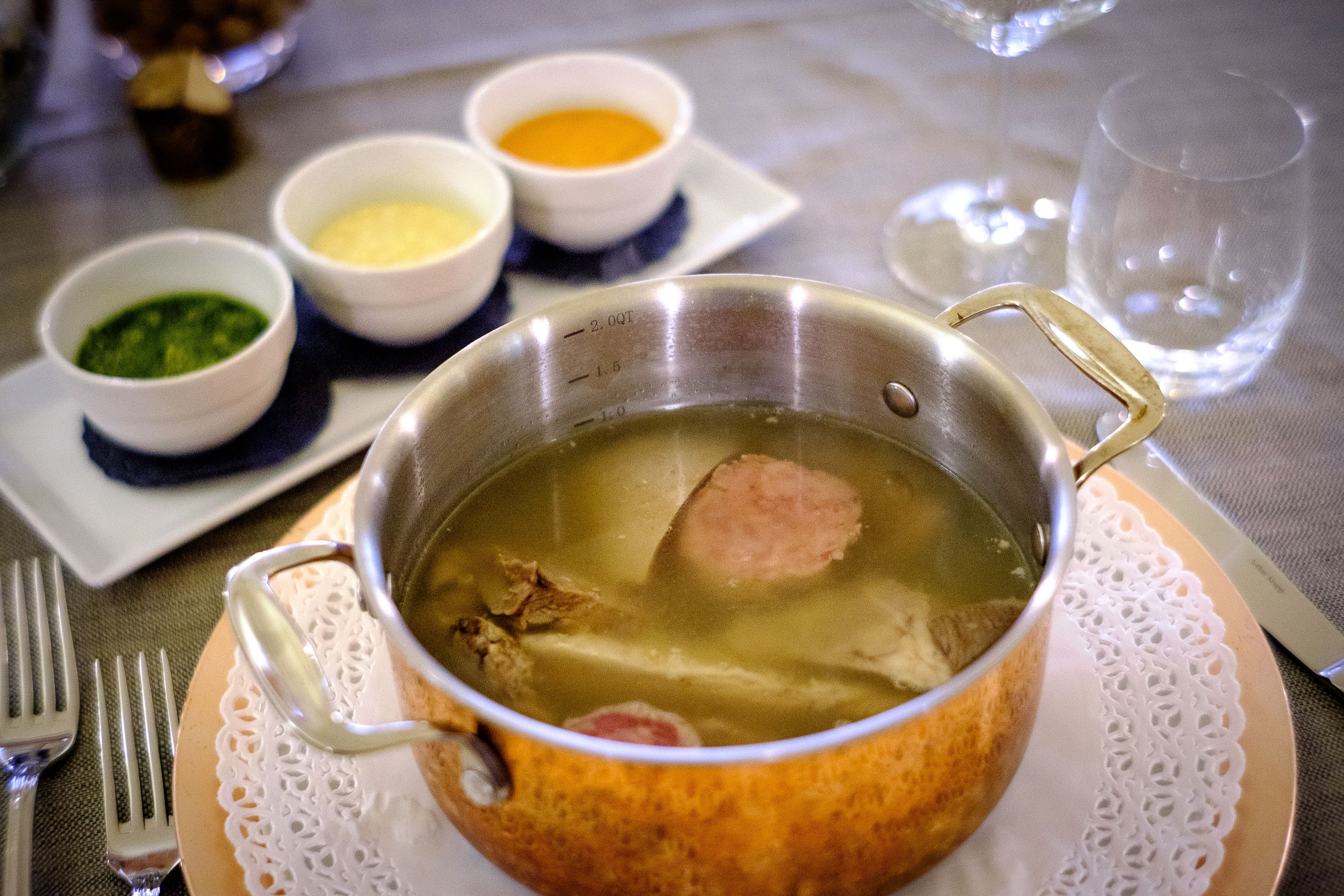 Een eettafel met een soepketel, verschillende kleine schaaltjes met toevoegingen en bestek.