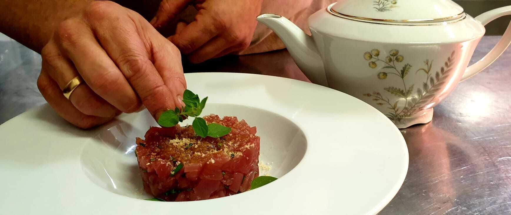 Une personne dépose une feuille de menthe sur une assiette de viande crue.