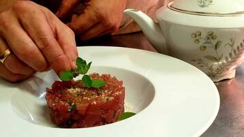 Une personne dépose une feuille de menthe sur une assiette de viande crue.