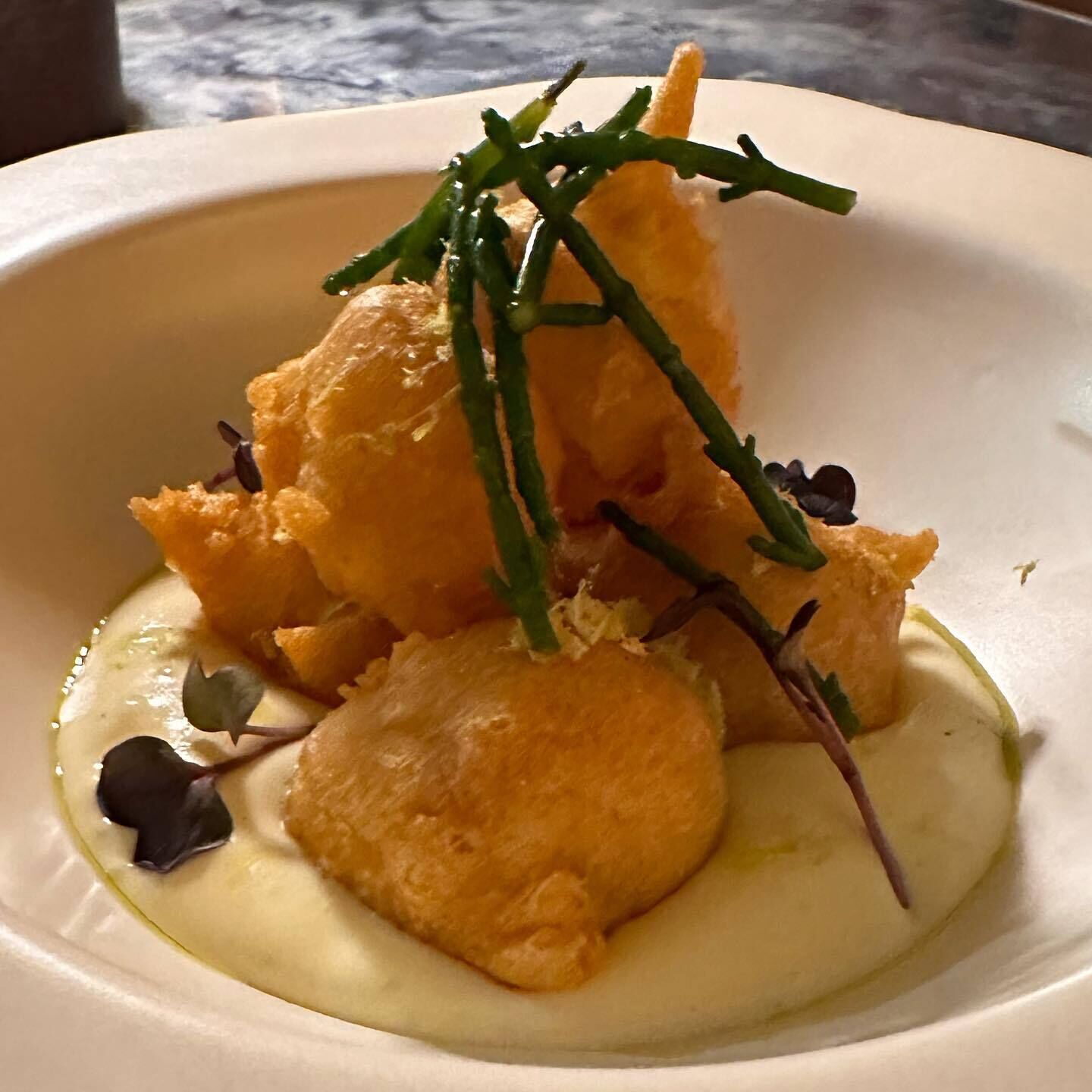 A dish with a creamy sauce, golden-brown croutons, and green garnish on a white plate.