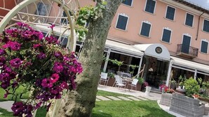 A building with a pink facade, a white awning, and a tree with purple flowers. - Ristorante Albergo Corona (Novi Ligure)