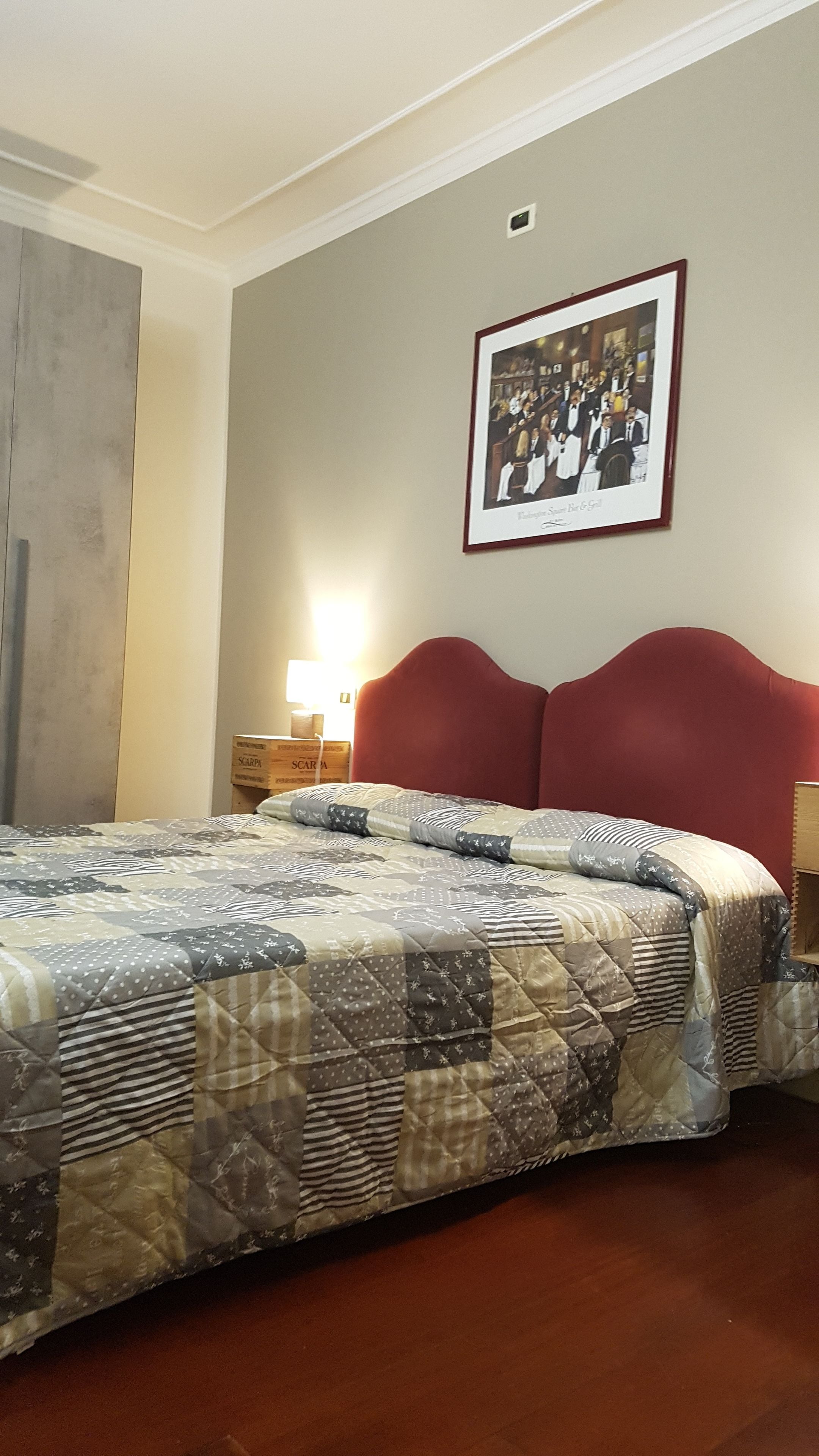 Ein Hotelzimmer mit einem großen Bett, einem roten Kopfteil, einem gerahmten Bild an der Wand und einem Nachttisch mit Lampe.