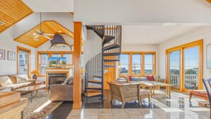 A spacious living area with a fireplace, a large window, and a staircase leading to an upper level. - Semi-Oceanfront Hatteras Home with Private Pool, Hot Tub, Game Room and Wet Bar (Hatteras)