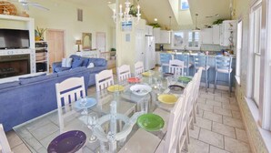 Amplia sala de estar con un sofá grande, una mesa de comedor preparada para seis personas y una zona de cocina con barra.