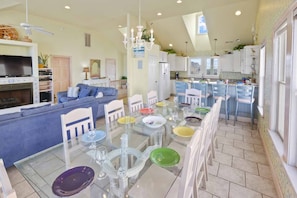 A spacious living room with a large sofa, a dining table set for six, and a kitchen area with a bar.